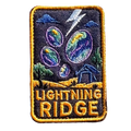 Lightning Ridge embroidered travel patch with colourful opals, lightning and a small mining shack beneath a dark sky; photographed on a transparent background.