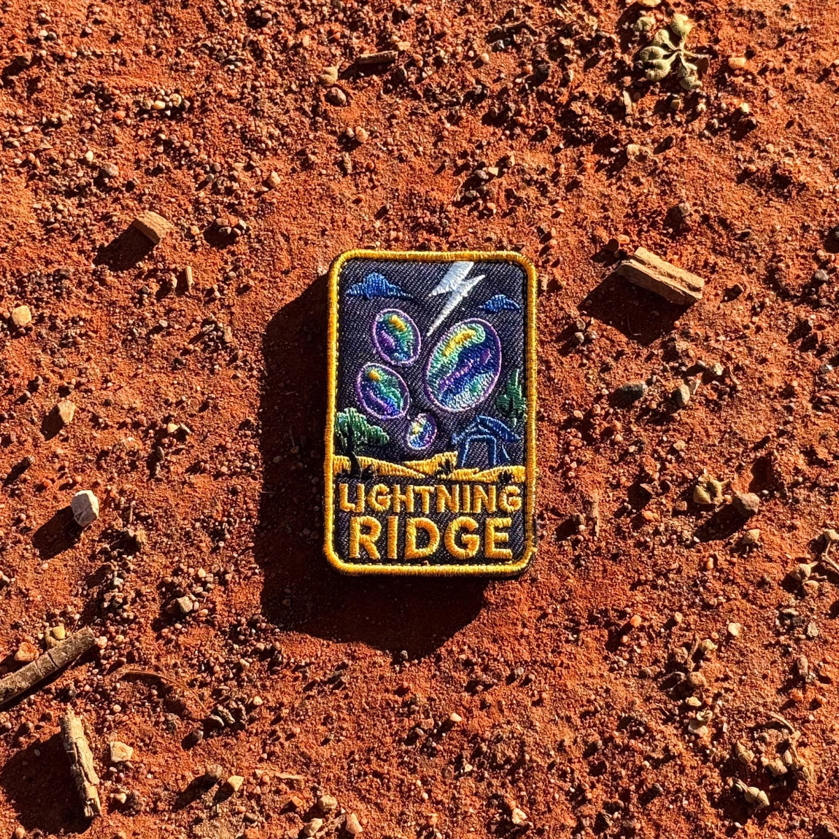 Lightning Ridge embroidered travel patch with colourful opals, lightning and a small mining shack beneath a dark sky.