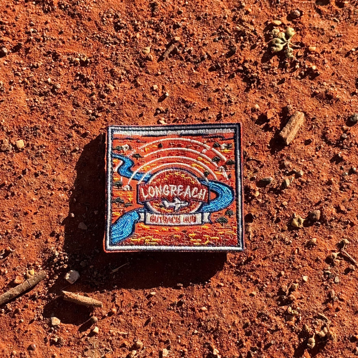 Longreach embroidered travel patch with a map-style outback landscape with a winding river, aircraft and Longreach Outback Hub lettering.