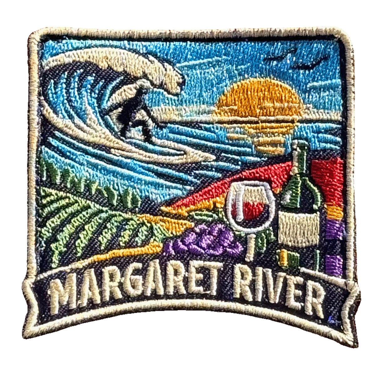 Margaret River embroidered travel patch with a surfer riding a wave above vineyard rows, grapes and a wine glass; photographed on a transparent background.