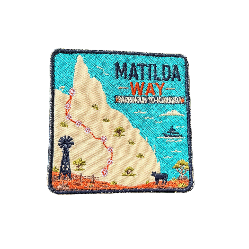 Matilda Way embroidered travel patch with a Queensland route map from Barringun to Kurumba, with a windmill, cattle and a boat; photographed on a transparent background.