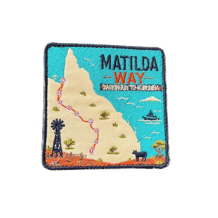 Matilda Way embroidered travel patch with a Queensland route map from Barringun to Kurumba, with a windmill, cattle and a boat; photographed on a transparent background.