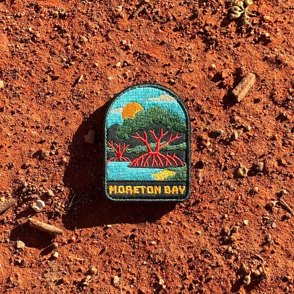 Moreton Bay embroidered travel patch with mangrove trees with exposed roots beside calm coastal water at sunset.