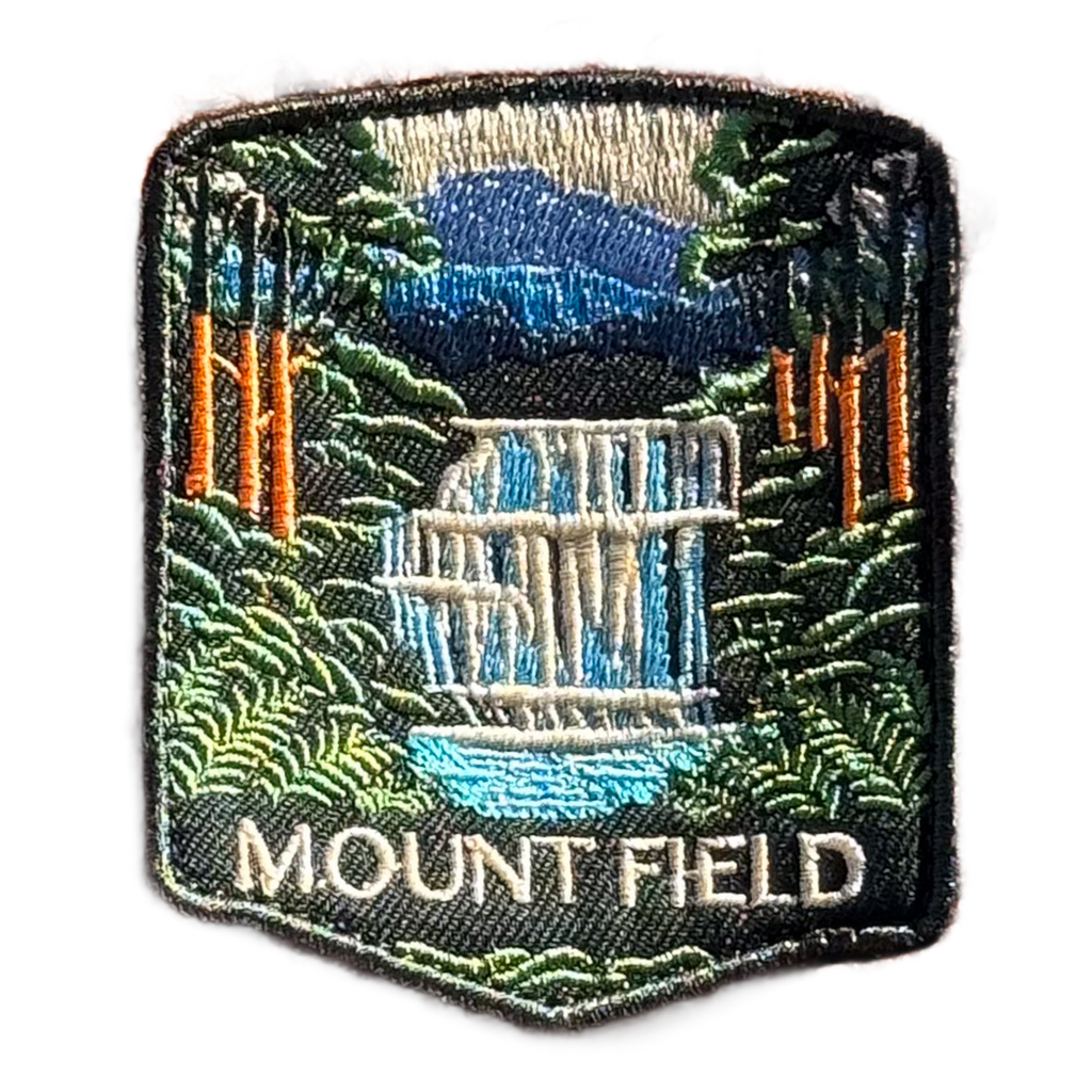 Mount Field National Park embroidered travel patch with a tiered waterfall surrounded by lush green forest; photographed on a transparent background.