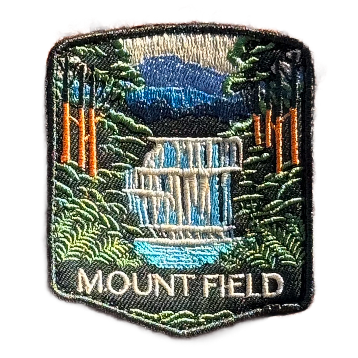 Mount Field National Park embroidered travel patch with a tiered waterfall surrounded by lush green forest; photographed on a transparent background.