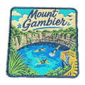 Mount Gambier embroidered travel patch with swimmers in a brilliant blue crater lake surrounded by limestone cliffs; photographed on a transparent background.