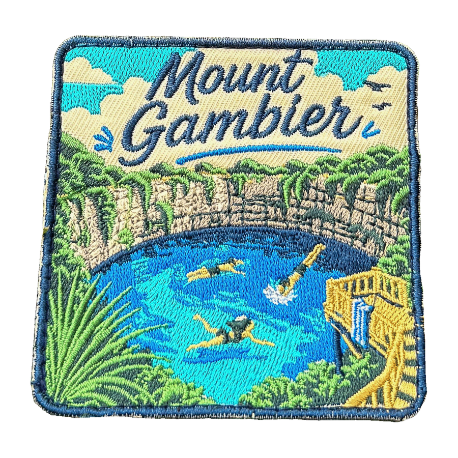 Mount Gambier embroidered travel patch with swimmers in a brilliant blue crater lake surrounded by limestone cliffs; photographed on a transparent background.