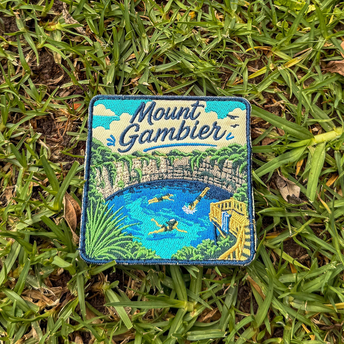 Mount Gambier embroidered travel patch with swimmers in a brilliant blue crater lake surrounded by limestone cliffs.