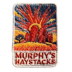 Murphys Haystacks embroidered travel patch with large rounded granite boulders in golden grass beneath a radiant sunset; photographed on a transparent background.