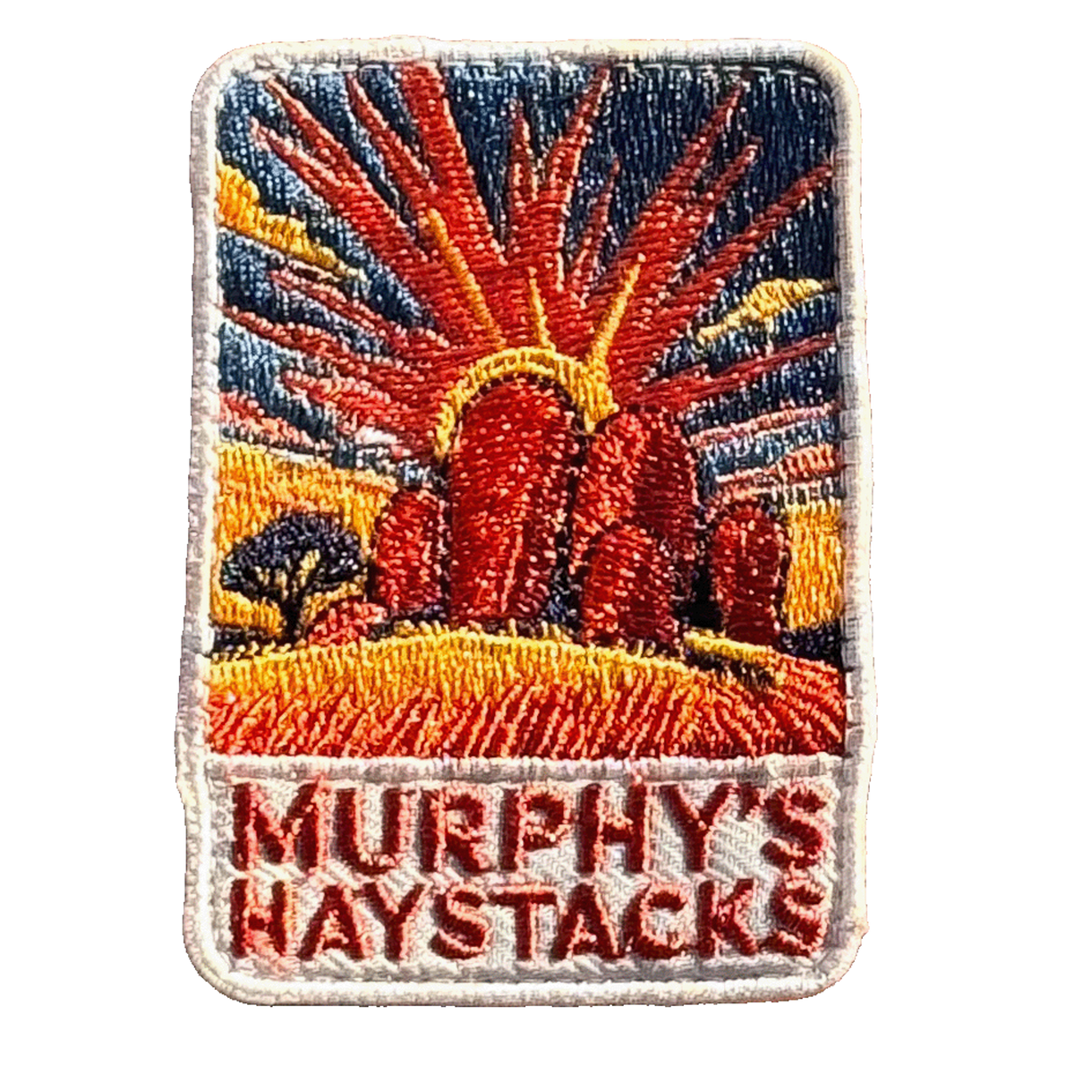 Murphys Haystacks embroidered travel patch with large rounded granite boulders in golden grass beneath a radiant sunset; photographed on a transparent background.