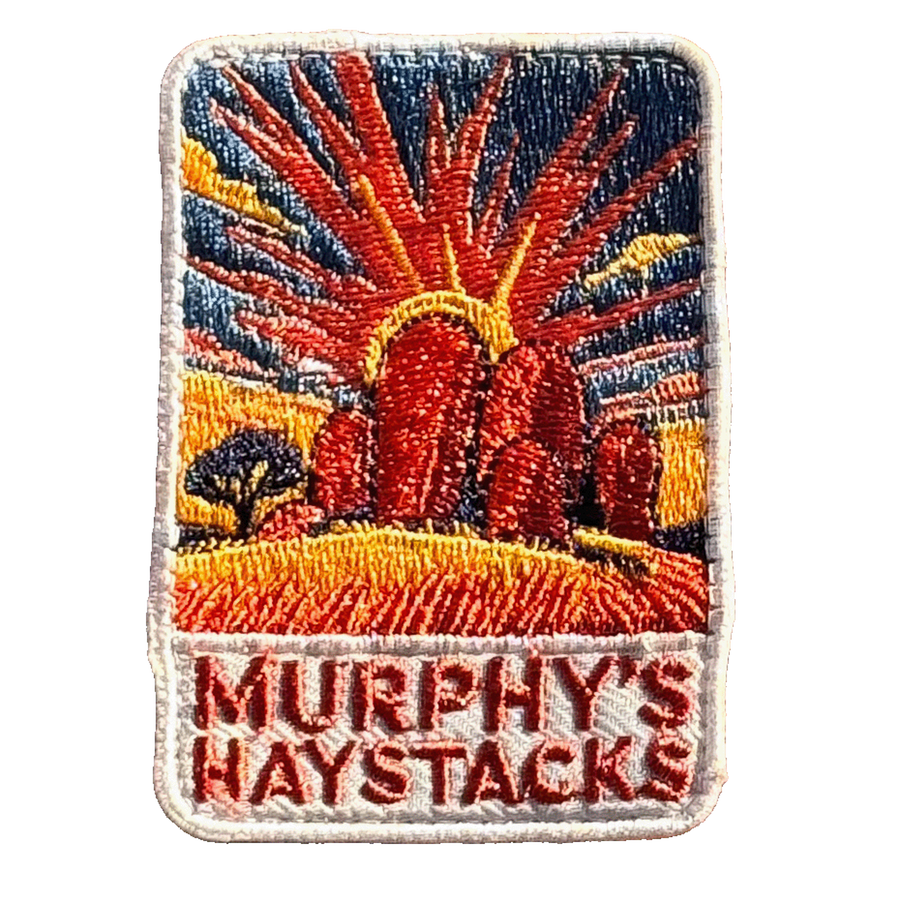 Murphys Haystacks embroidered travel patch with large rounded granite boulders in golden grass beneath a radiant sunset; photographed on a transparent background.