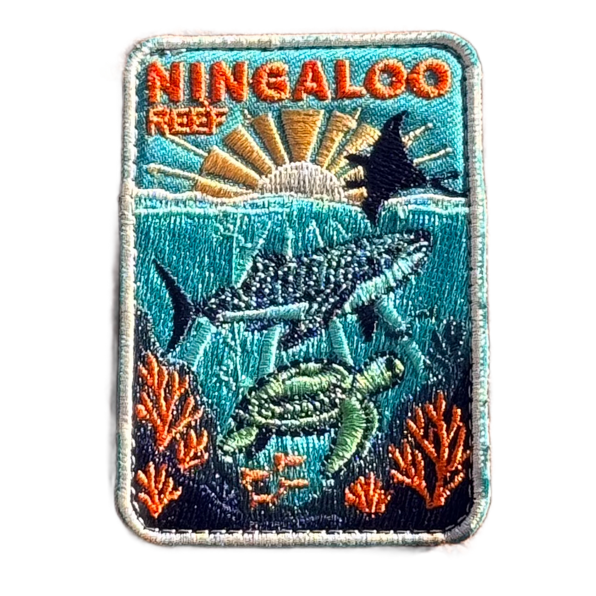 Ningaloo Reef embroidered travel patch with a whale shark, manta ray and sea turtle swimming over coral reef; photographed on a transparent background.