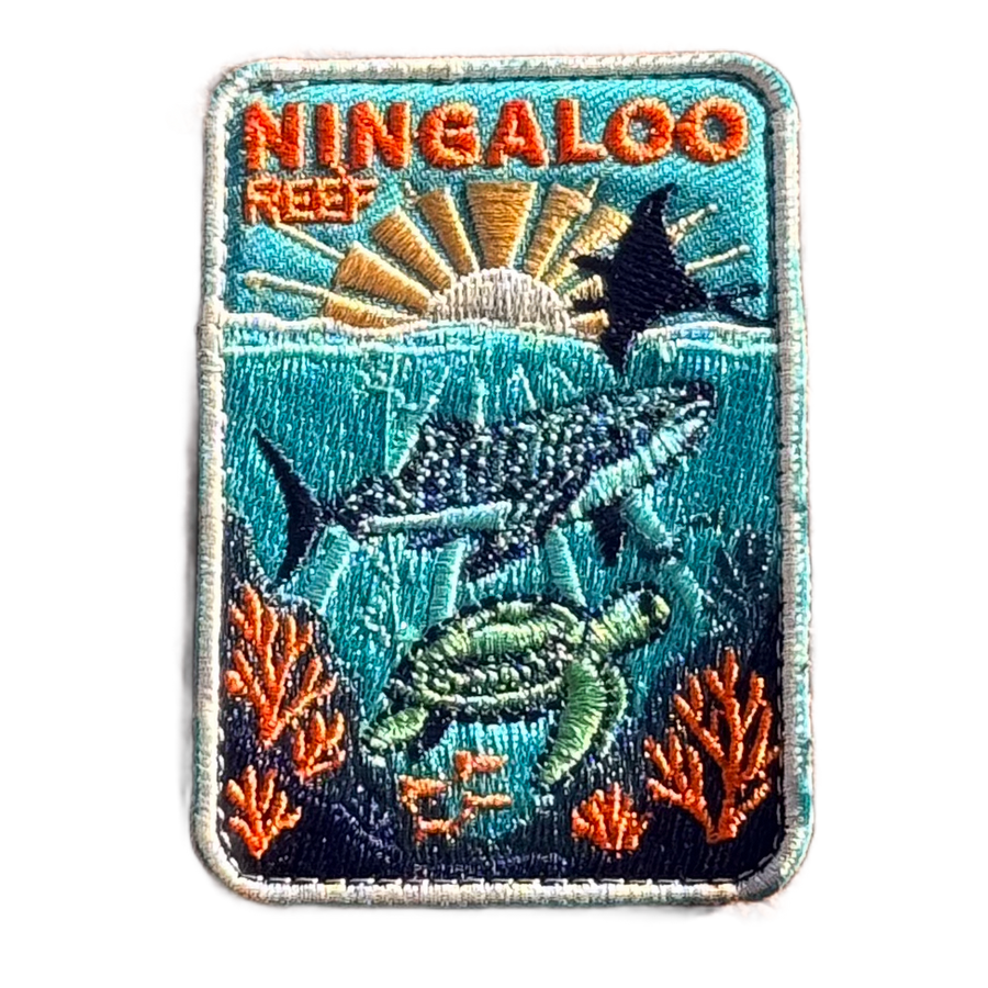Ningaloo Reef embroidered travel patch with a whale shark, manta ray and sea turtle swimming over coral reef; photographed on a transparent background.