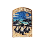 Phillip Island embroidered travel patch with three little penguins on a beach with a motorcycle racer and ocean cliffs behind; photographed on a transparent background.