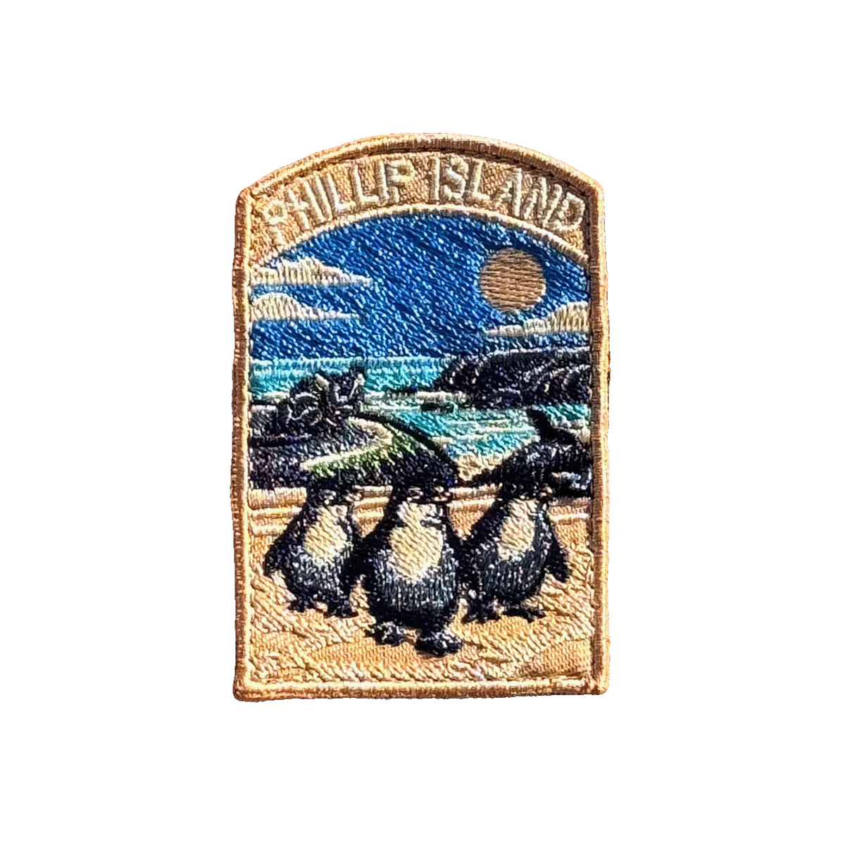 Phillip Island embroidered travel patch with three little penguins on a beach with a motorcycle racer and ocean cliffs behind; photographed on a transparent background.