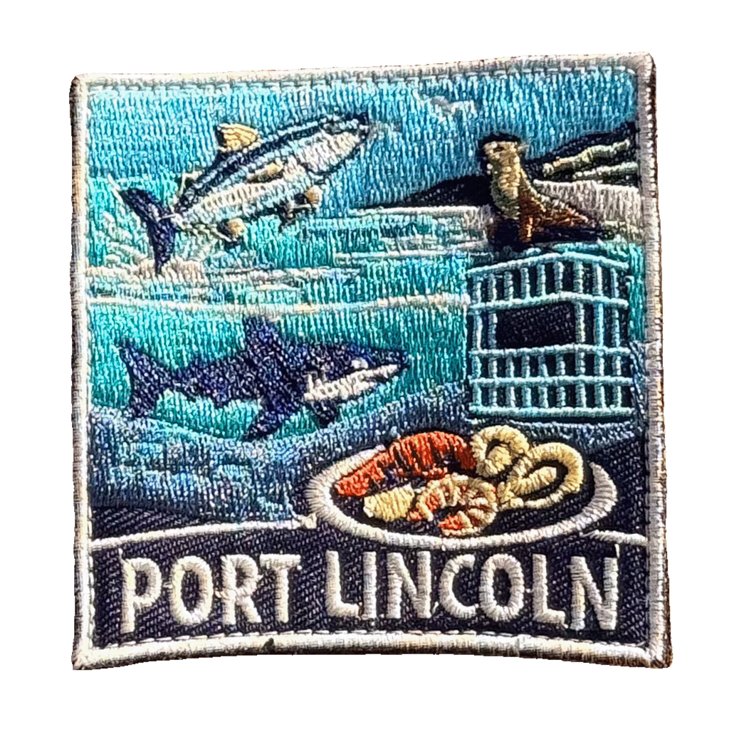 Port Lincoln embroidered travel patch with a tuna, great white shark, sea lion, cage-diving cage and seafood platter; photographed on a transparent background.