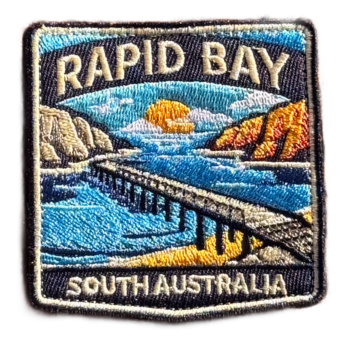 Rapid Bay embroidered travel patch with a long jetty above turquoise coastal water; photographed on a transparent background.