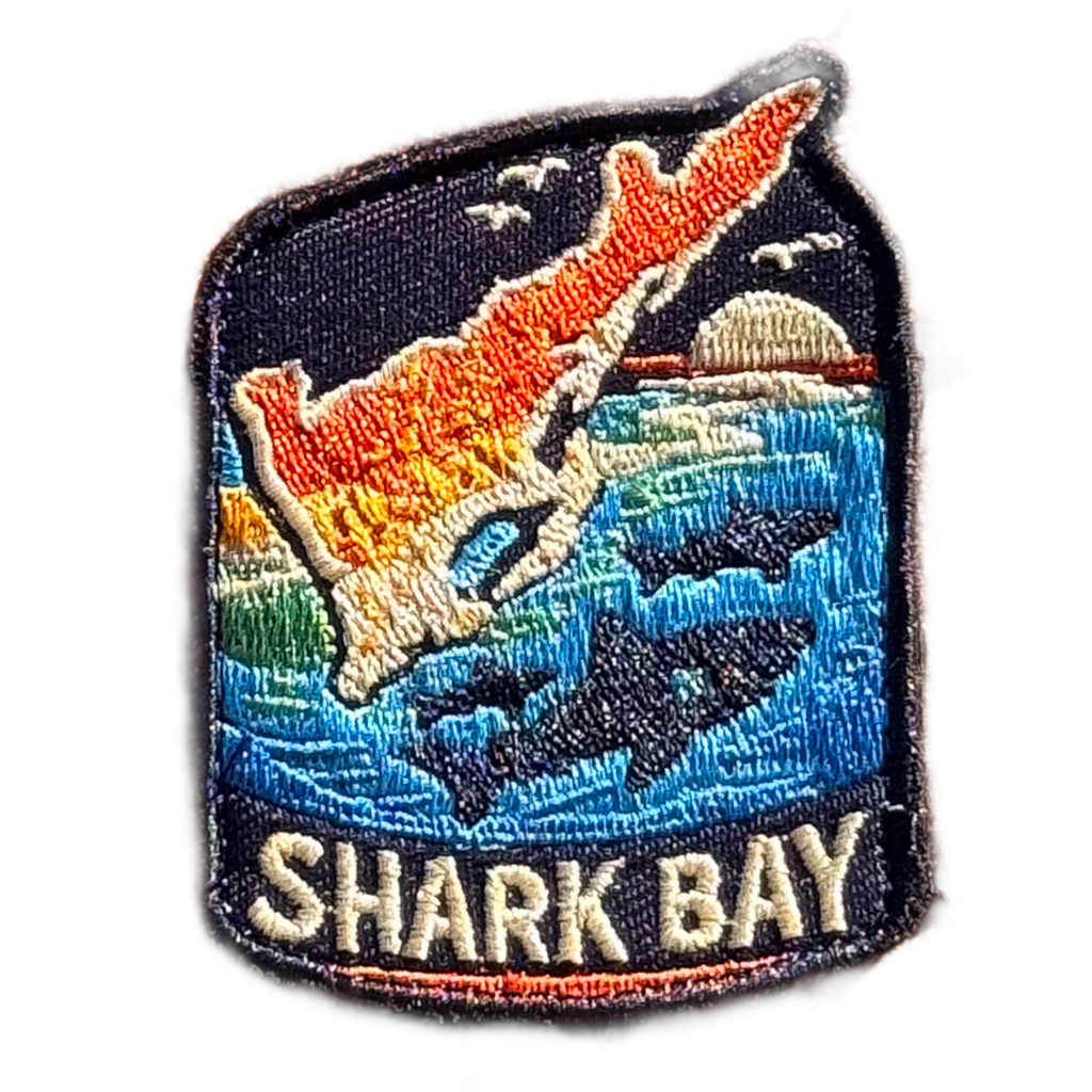 Shark Bay embroidered travel patch with a marine coastline with turquoise water and sea life; photographed on a transparent background.