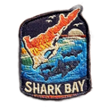 Shark Bay embroidered travel patch with a marine coastline with turquoise water and sea life; photographed on a transparent background.