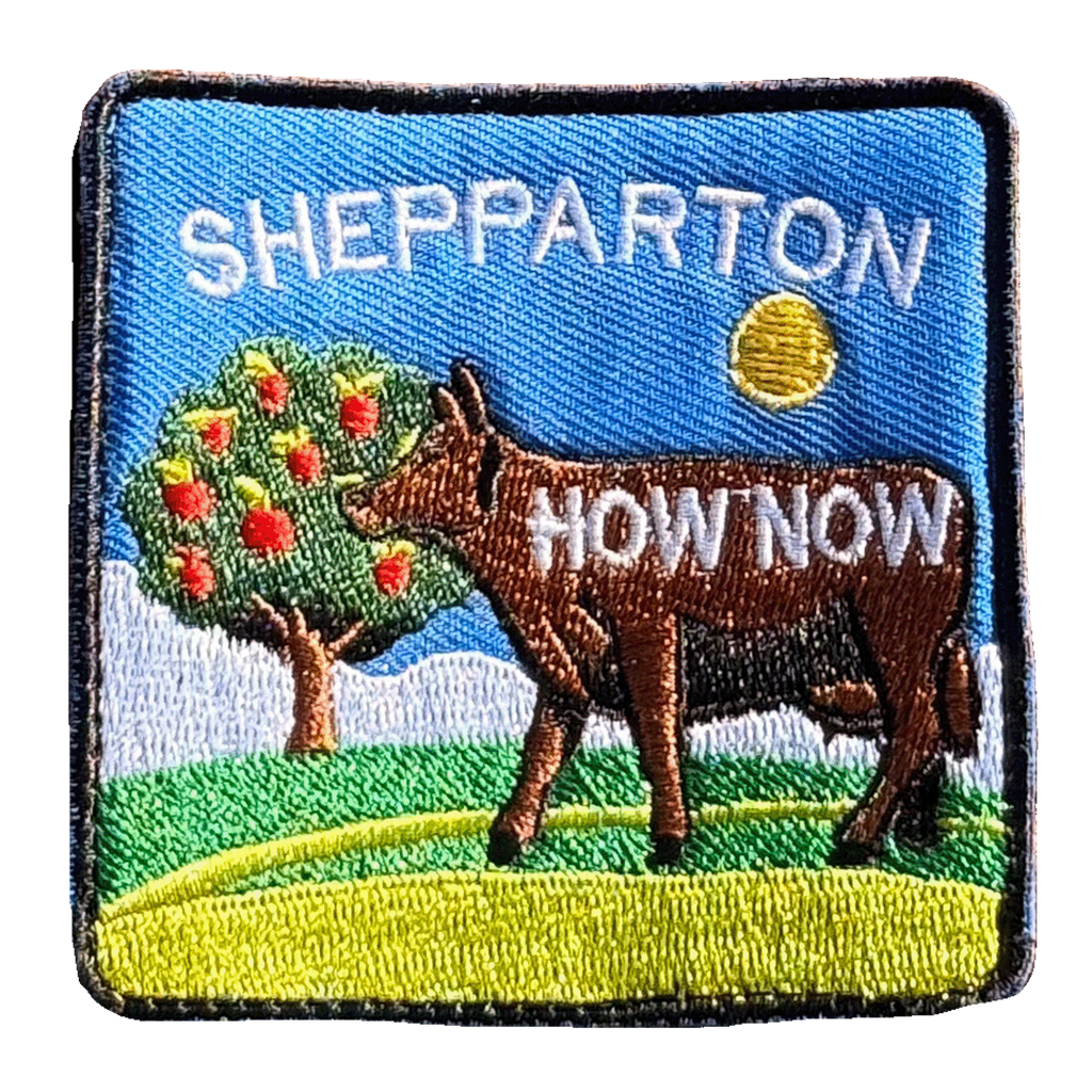 Shepparton embroidered travel patch with a colourful cow sculpture in a regional landscape; photographed on a transparent background.
