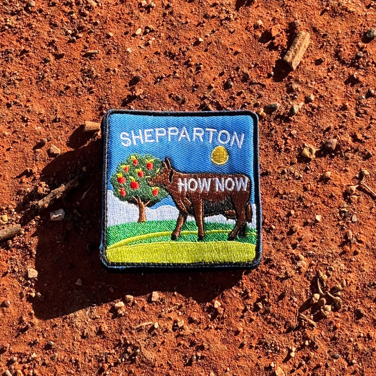 Shepparton embroidered travel patch with a colourful cow sculpture in a regional landscape.