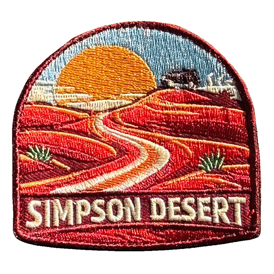 Simpson Desert embroidered travel patch with a four-wheel drive crossing red desert sand dunes; photographed on a transparent background.