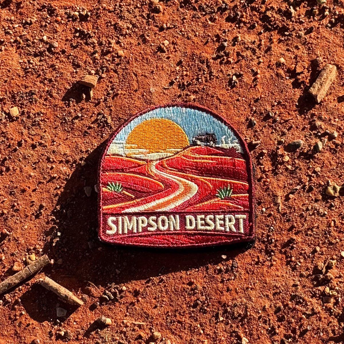Simpson Desert embroidered travel patch with a four-wheel drive crossing red desert sand dunes.