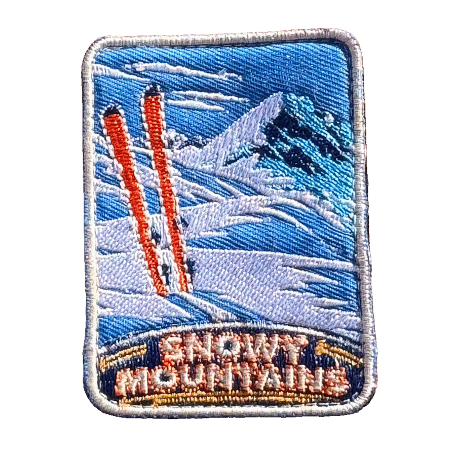 Snowy Mountains embroidered travel patch with snow-covered alpine peaks; photographed on a transparent background.