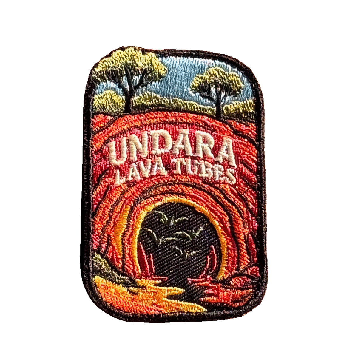 Undara Lava Tubes embroidered travel patch with a lava tube cave opening in an outback landscape; photographed on a transparent background.