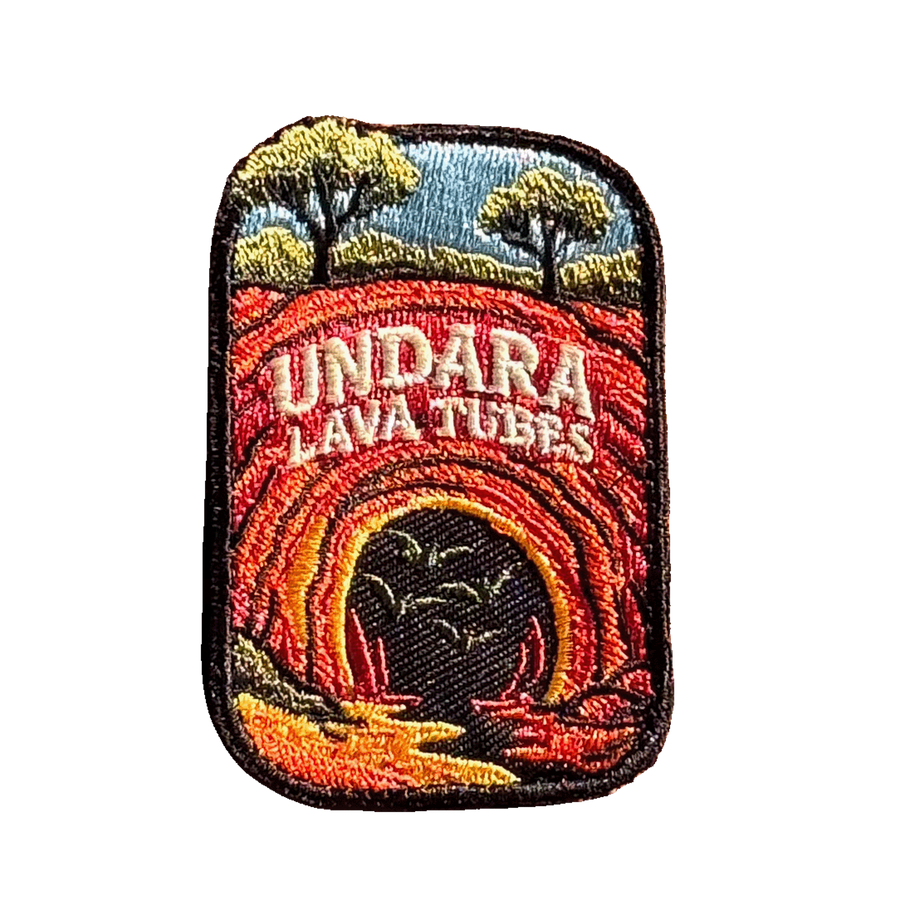 Undara Lava Tubes embroidered travel patch with a lava tube cave opening in an outback landscape; photographed on a transparent background.