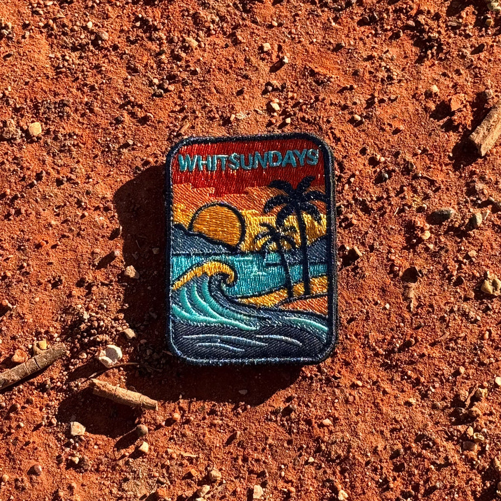 Whitsundays embroidered travel patch with a tropical island beach with palm trees, curling wave and sunset.