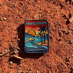 Whitsundays embroidered travel patch with a tropical island beach with palm trees, curling wave and sunset.