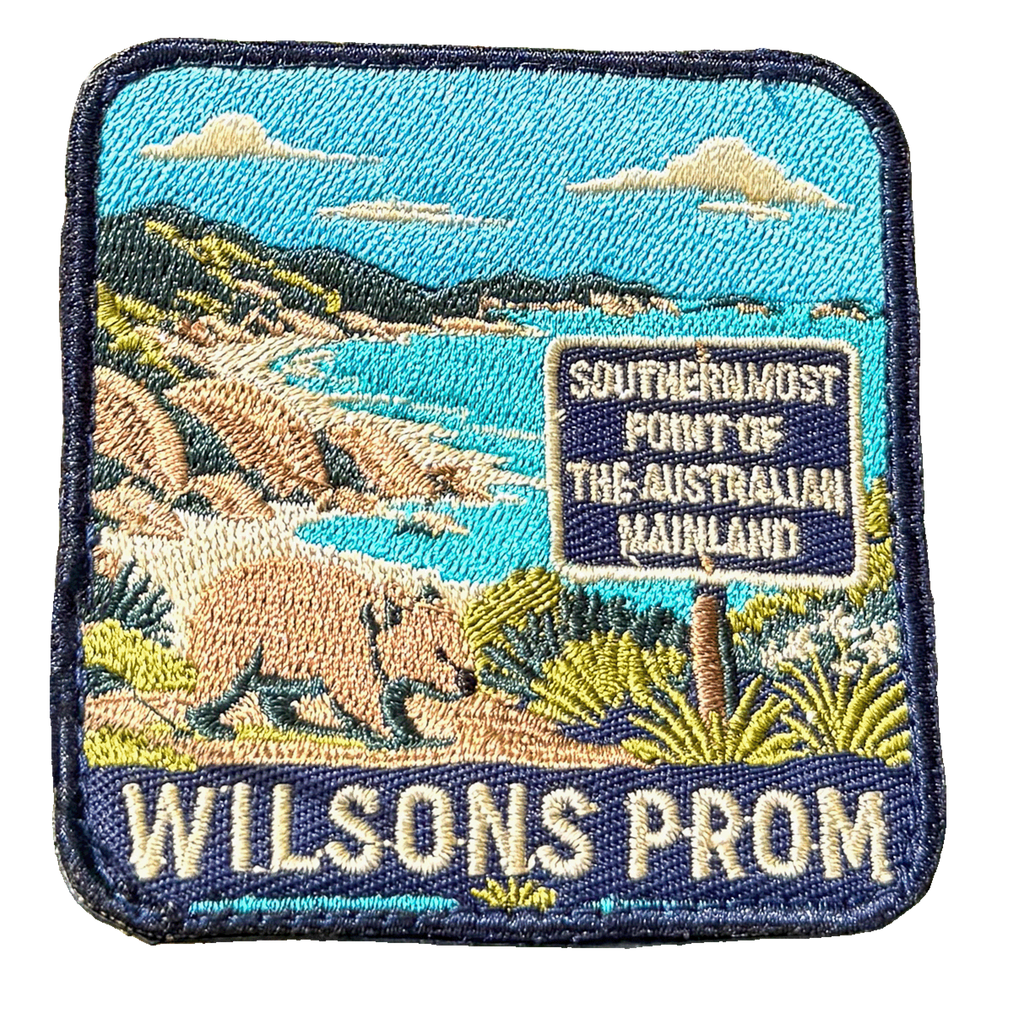 Wilsons Promontory embroidered travel patch with a wombat beside the southernmost point of mainland Australia sign and coastal bay; photographed on a transparent background.