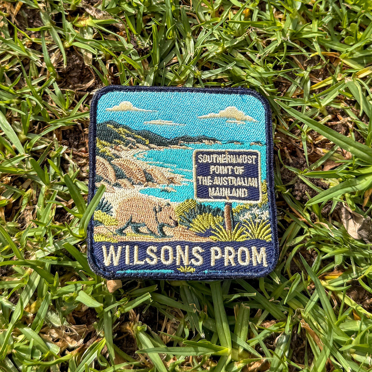Wilsons Promontory embroidered travel patch with a wombat beside the southernmost point of mainland Australia sign and coastal bay.