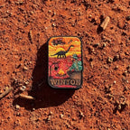Winton embroidered travel patch with a dinosaur, vintage aircraft and traveller sitting beside a campfire at sunset.