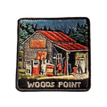 Woods Point embroidered travel patch with a rustic high-country petrol station with old fuel pumps among pine trees; photographed on a transparent background.