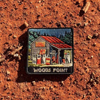 Woods Point embroidered travel patch with a rustic high-country petrol station with old fuel pumps among pine trees.