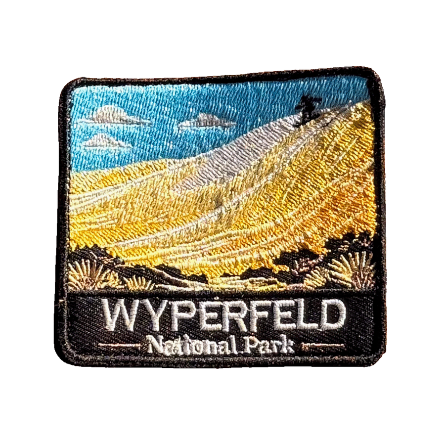 Wyperfeld National Park embroidered travel patch with a sandboarder on a towering pale sand dune above scrubland; photographed on a transparent background.